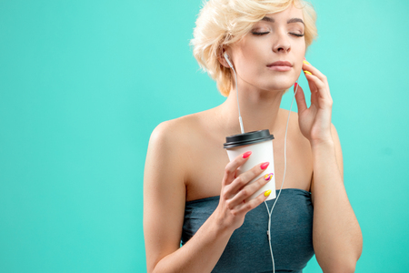 awesome blond girl enjoying listening to music while drinking coffeeの写真素材