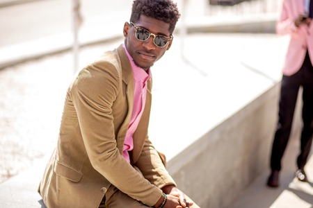 Young afro american man in suit sitting in the street on a sunny dayの写真素材