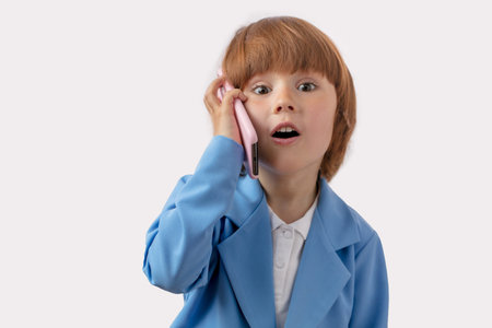 a surprised little boy in elegant stylish suit with mobile phone