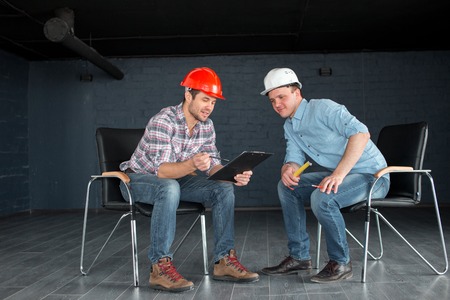 two talented workers in hardhats are looking at the documentsの写真素材