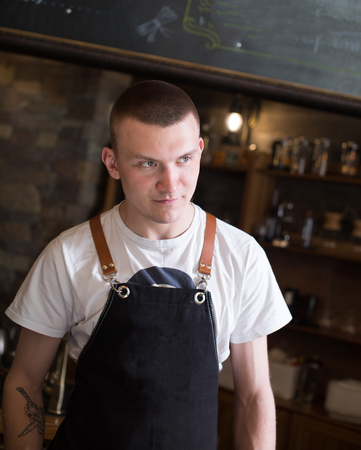 Portrait of young handsome man wearing an apron standing in a coffee shop.の写真素材