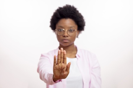 serious afro woman in glasses making stop gesture. Don't smoke. stop talking, keep silence. pay attention , note, warning concepts. focus on the palm. blurred background. hypnosisの写真素材