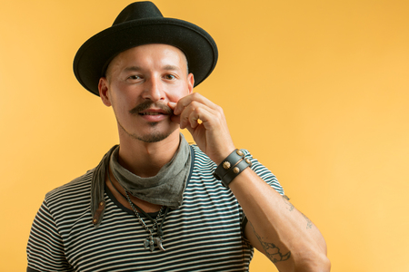 Happy man with moustache wearing hat isolated over yellow background.の写真素材