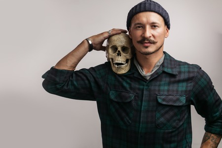 Stylish man with mustache wearing hat and holding scull posing indoorsの写真素材
