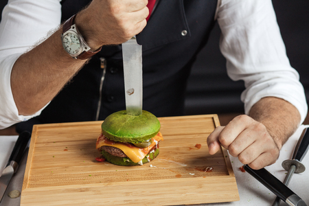 Process of eating burgers. Master Cook cutting tasty hamburger with spinach bunの写真素材