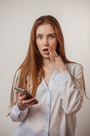 Young emotional attractive redhead female holding smartphone isolated at studioの写真素材