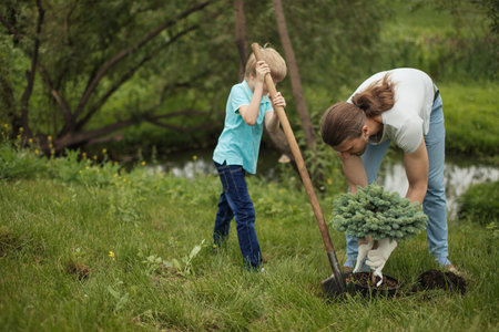 Smiling adult father and his son planting a tree outdoors in park.