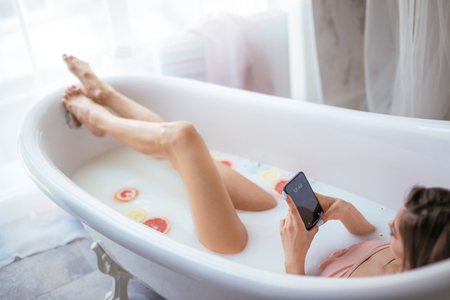 High angle view of unrecognizable pretty woman using smartphone while having a milky moisturising bath at homeの写真素材