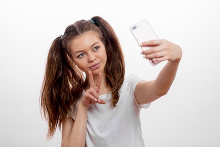 smiling young woman dressed casually showing two fingers while taking a photoの写真素材