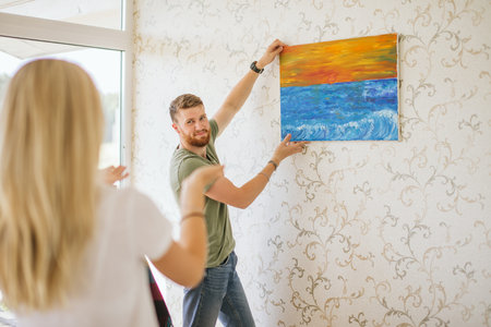 Moving house. Couple hanging picture on wall in new home