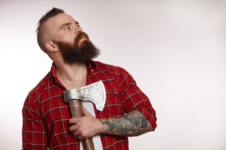 bearded male holding axe on chest and posing in studioの写真素材