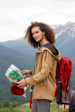 Man Traveler with map and red backpack searching location outdoor with rocky mountains on backgroundの写真素材