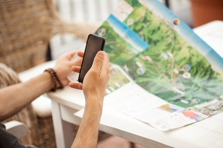guy traveler planning trip for vacation with smartphone and map while sitting at cafeの写真素材
