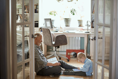 Grandpa looks photo album with his wedding, little boy using electronic tablet