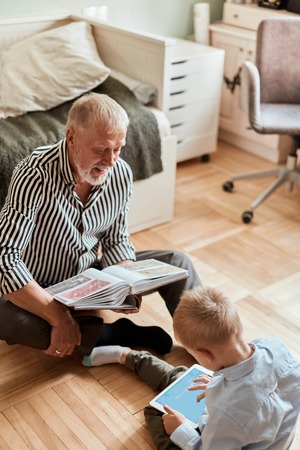 Grandpa looks photo album with his wedding, little boy using electronic tabletの写真素材