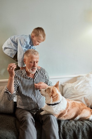 Grandfather and grandson with dog sitting at couch in roomの写真素材