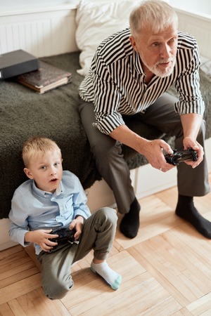 Grandfather and grandson playing video games on computer with joystickの写真素材