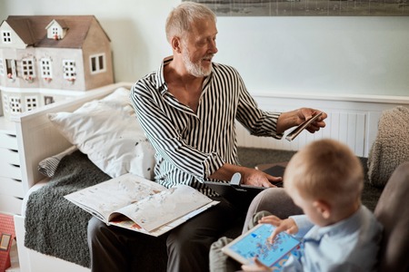 Grandpa looks photo album with his wedding, little boy using electronic tabletの写真素材
