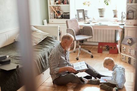 Grandpa looks photo album with his wedding, little boy using electronic tabletの写真素材