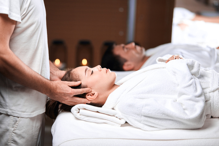 Beautiful young woman receiving massage on head and shoulders zone in spa centreの写真素材