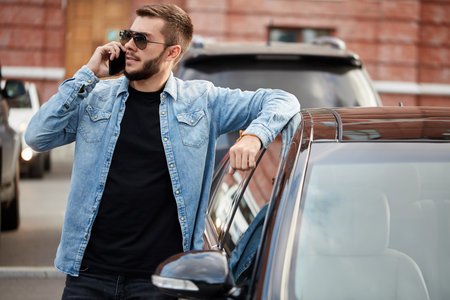 cool young man is talking on the smart phone while standing near the car