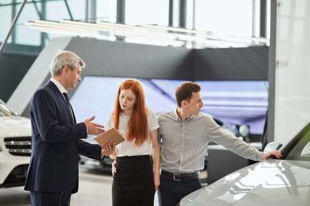 Car sales manager telling about the features of the car to the customers at the dealershipの写真素材