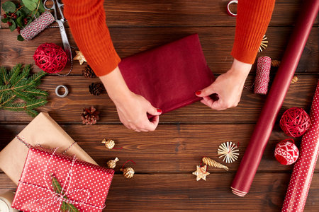 Female hands decorating gift red boxes for Christmas Holiday. Hands close up. Present packaging...