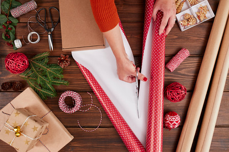 Woman wrapping gift box with decorating items on wood table, close up, top view.の写真素材