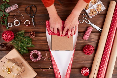 Woman s hands wrapping Christmas gift on dark wooden background.の写真素材