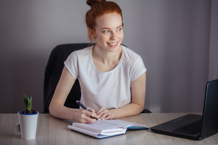 Portrait of redhaired young woman with laptop sitting at the tab