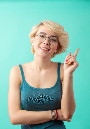 Blonde woman pointing up with forefinger, isolated on blueの写真素材