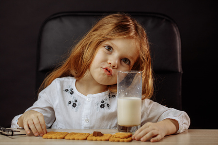 Happy beautiful little girl having a snack with milk and cookiesの写真素材