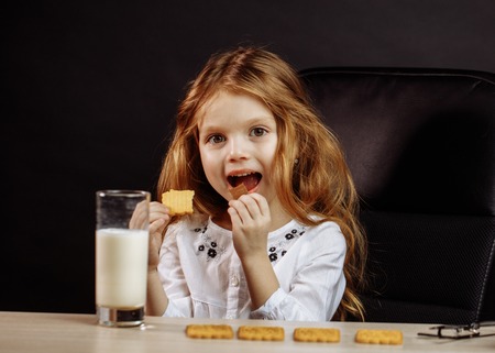 Happy beautiful little girl having a snack with milk and cookiesの写真素材