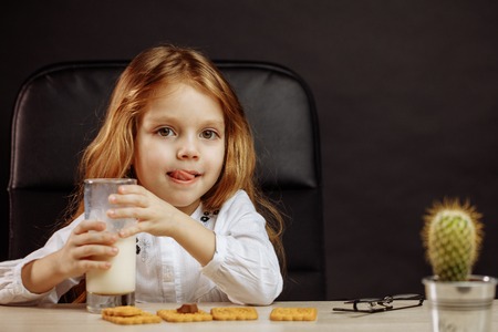 Happy beautiful little girl having a snack with milk and cookiesの写真素材