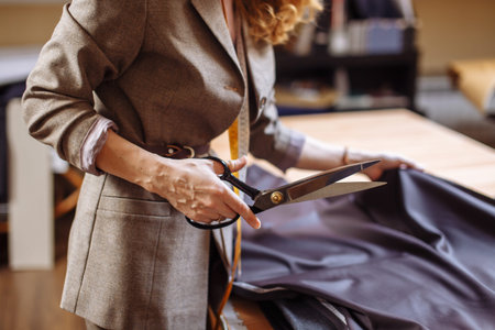 Female fashion designer working on suiting fabric with dressmaking accessories on table