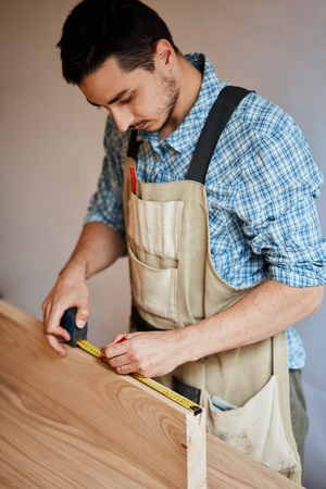 hand of a carpenter taking measurement of a wooden plankの写真素材
