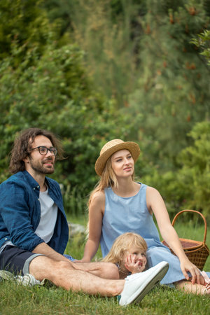 happy Family picnicking outdoors with their cute daughter, blue clothes, woman in hat