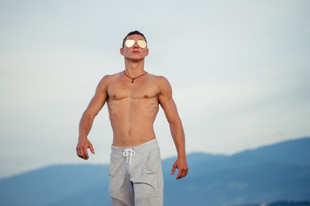 Masculine body man in sunglasses at beach with mountauns on backgroundの写真素材