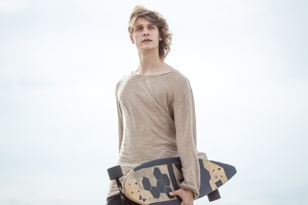 Stylish man stands on street and hold long board in handsの写真素材