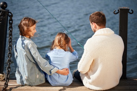 happy family with daughter fishing in pond in fallの写真素材