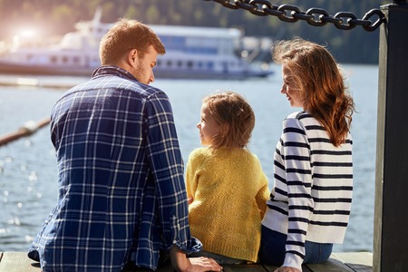 rear view of family sit on pier in autumn day. Fall family portraitの写真素材