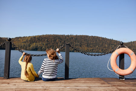 rear view mother and daughter sitting on pier warm autumn dayの写真素材
