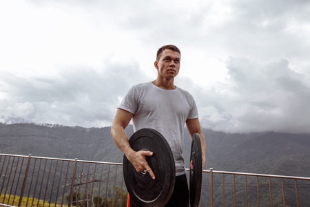 Stong male athlete pumping musculs with weight plates in outdoor workout.の写真素材