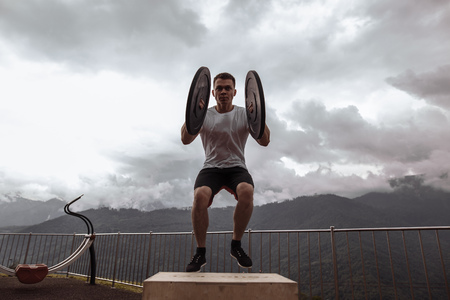 Strong male athlete doing box jumps with two plates outdoor on top of mountain.の写真素材
