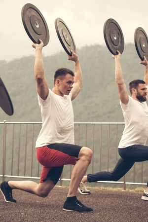 two athletes with barbell disc making lunges in outdoor workoutの写真素材