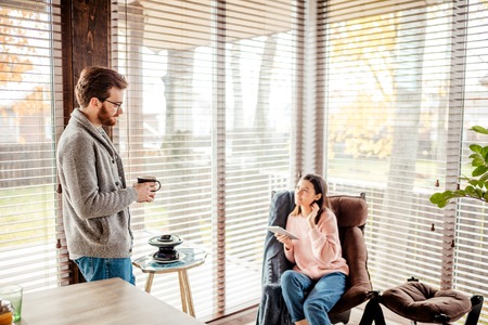 Couple in kitchen spending time together with cup of coffee and smartphoneの写真素材