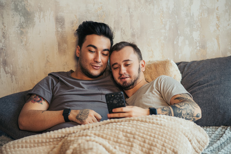 Happy gay couple taking selfie on bed at homeの写真素材