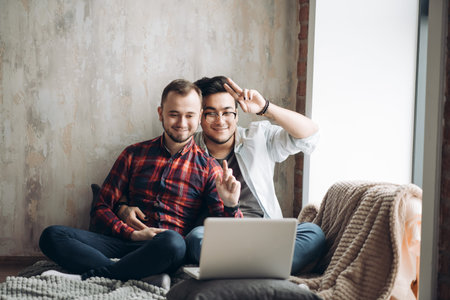 European gay male couple spend time together drinking coffee and watching laptop