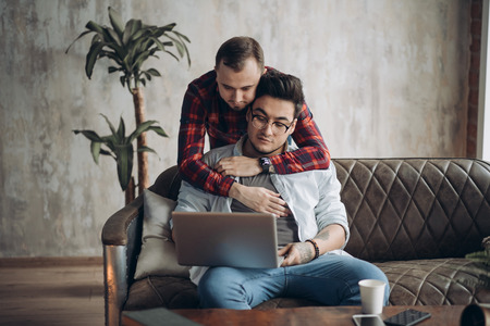 European gay male couple spend time together drinking coffee and watching laptopの写真素材