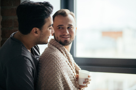 two handsome homosexual guys while standing near windowの写真素材